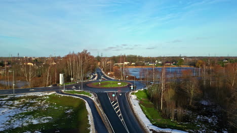 aerial drone forward moving shot over road crossing surrounded by patches of snow on a cold winter morning