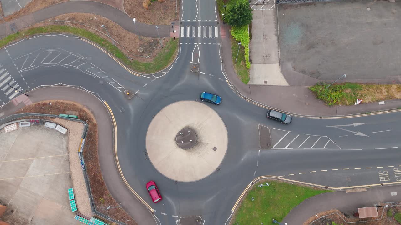 An aerial view of a roundabout with cars navigating the lanes. The clear road markings and surrounding greenery highlight efficient urban planning and traffic management