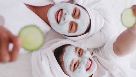 video de madre y hija asiáticas felices en túnicas haciendo máscara de pepino y divirtiéndose