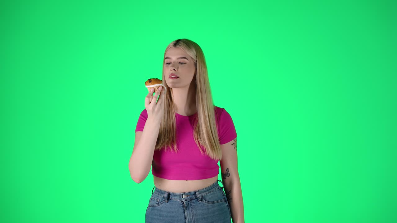 초록색 배경에 머핀 페이스트리를 벗고 먹는 젊은 예쁜 여성의 초상화, 스튜디오 촬영