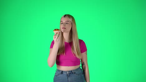 Portrait-Of-Young-Pretty-Woman-Unwraps-and-Eating-Muffin-Pastry-Against-Green-Background,-Studio-Shot