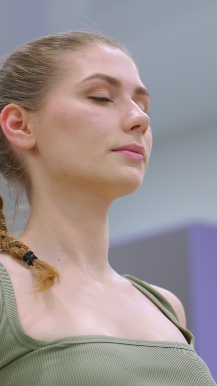 mujer enfocada realizando un ejercicio de flexibilidad de la columna vertebral en una pelota de ejercicio verde, ojos cerrados, profundamente inclinada hacia atrás, con un supervisor desinteresado en el fondo
