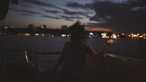 beautiful young woman dances on the deck of a ship with bengal lights at night. woman having fun time