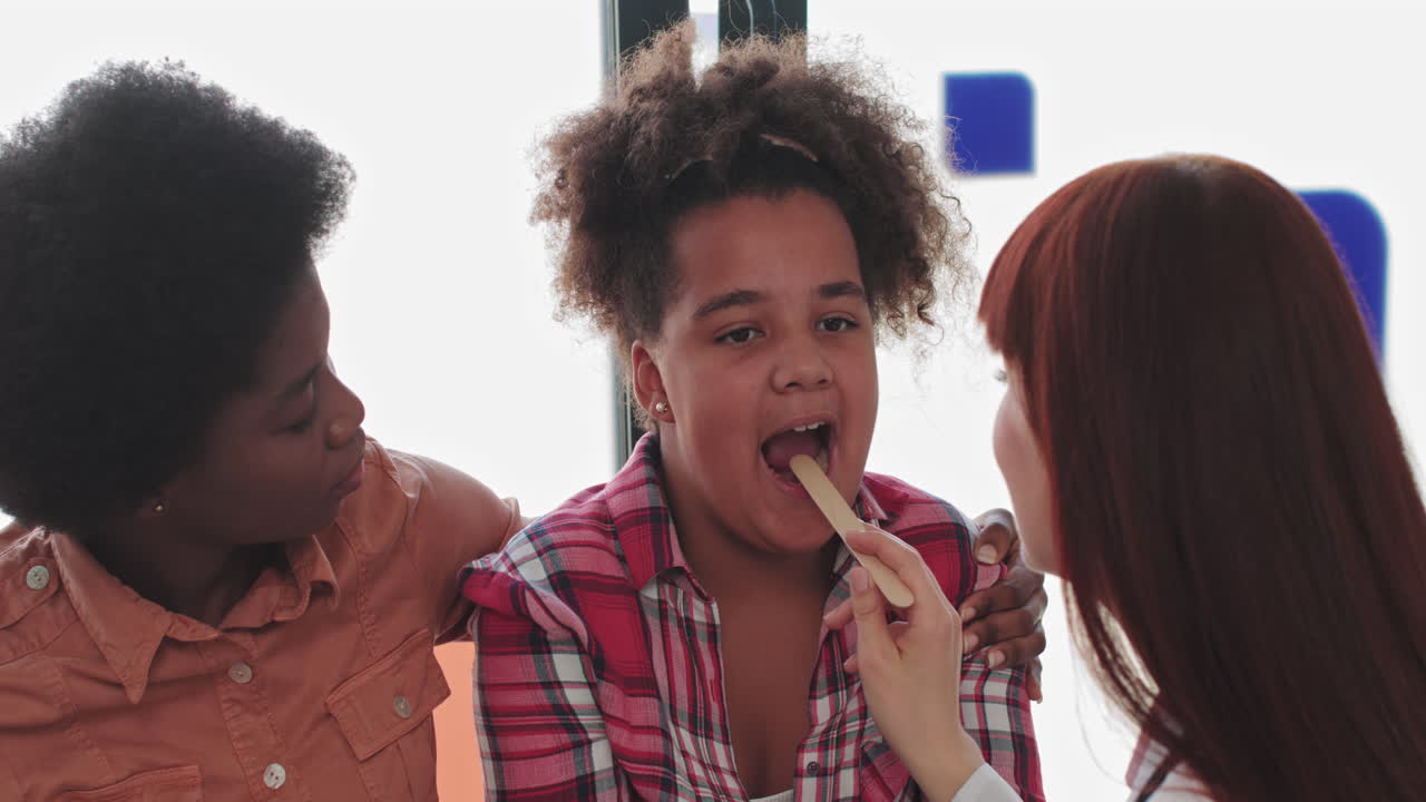 Young female doctor examines babys throat little girl with mother at pediatricians reception child