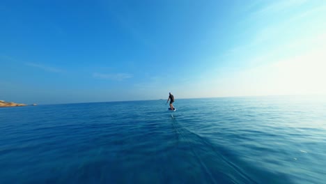 aerial view of a young man riding a new type of renewable green water craft technology called an electric hydrofoil, man gliding over glassy ocean water on a hydrofoil, the future of ocean travel