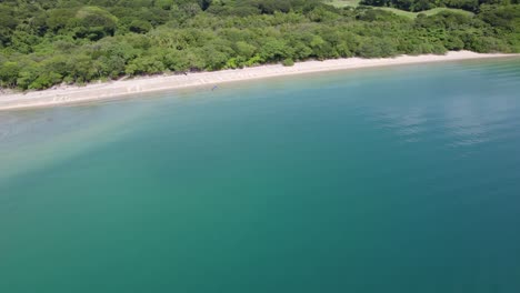 aerial rising over turquoise sea, sand shore and dense green woods coast in nacascolo beach, papagayo peninsula, costa rica