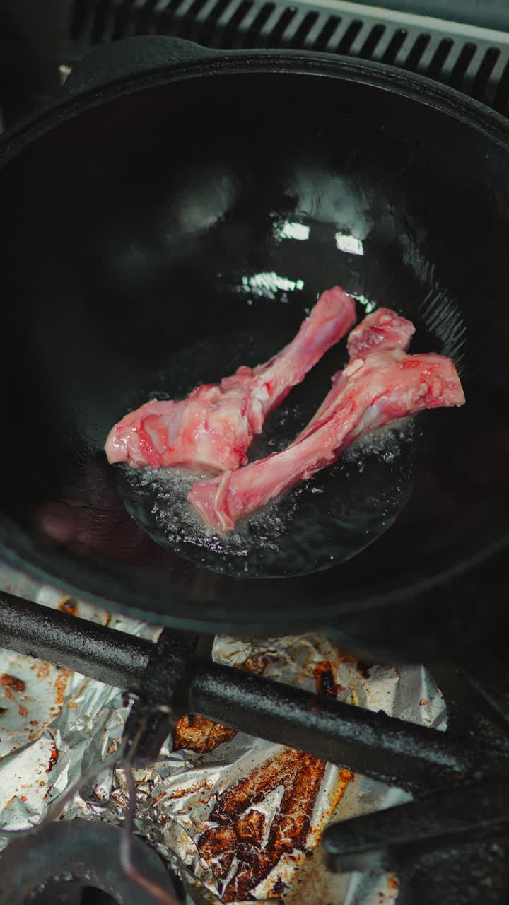 Memasukkan Tulang Daging Mentah ke dalam Air Mendidih di Panci Hitam