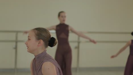 un grupo de jóvenes estudiantes de ballet con ropa de baile negra practicando posiciones en un amplio estudio de ballet con pisos de madera y barras montadas en la pared. expresiones enfocadas y movimientos sincronizados.