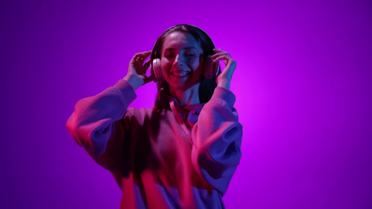 ragazza felice e sorridente che ascolta musica con le cuffie e balla su uno sfondo viola alla luce del neon, filtro. 4k. emozioni, pubblicità, cultura, concetto giovanile