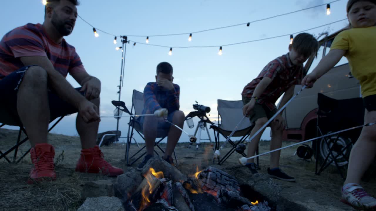 Laughing family frying marshmellow on bonfire