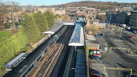 filmische drohnenaufnahmen aus der luft eines zuges, der den bahnhof mit bahnsteig und parkplatz verlässt, dewsbury, west yorkshire, großbritannien