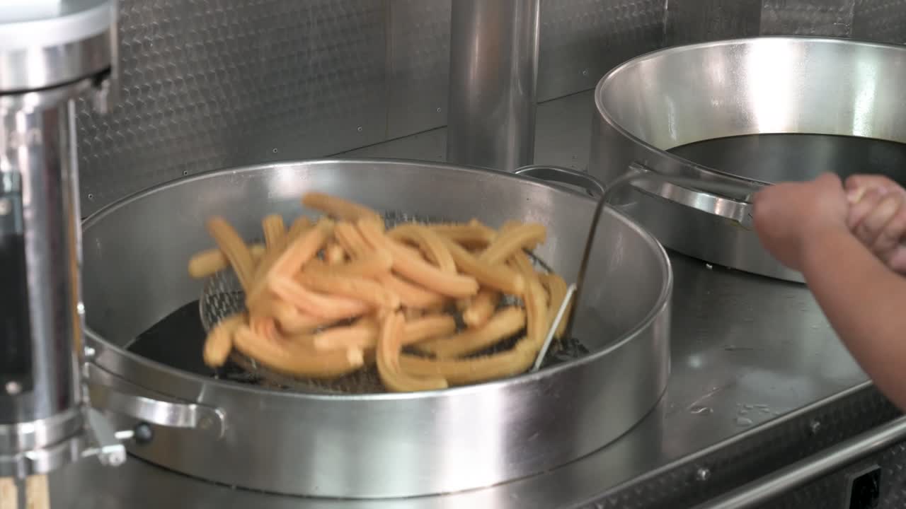 En portion churros tilberedes til perfektion ved hjælp af en kommerciel churrosmaskine og frituregryde. Denne scene illustrerer fødevareproduktionsprocessen i et specialiseret spansk spisested.
