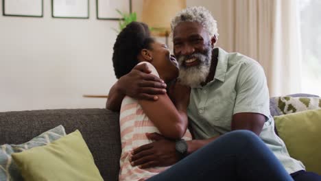 Happy-african-american-couple-sitting-on-couch-embracing-and-smiling