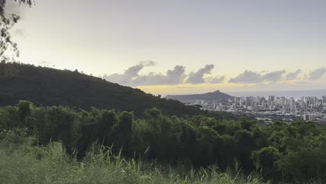 A-breathtaking-view-of-Honolulu's-skyline-at-sunset,-with-the-iconic-Diamond-Head-in-the-distance,-framed-by-lush-greenery