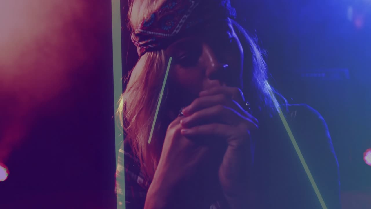 Cantante donna che tiene un microfono e canta sul palco, barre al neon che illuminano il volto, bandana in vista