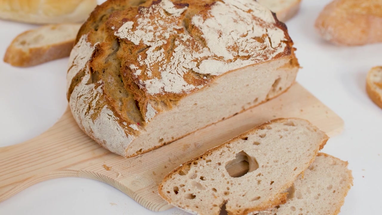 A hand picks up a slice of crusty sourdough bread from a wooden board.