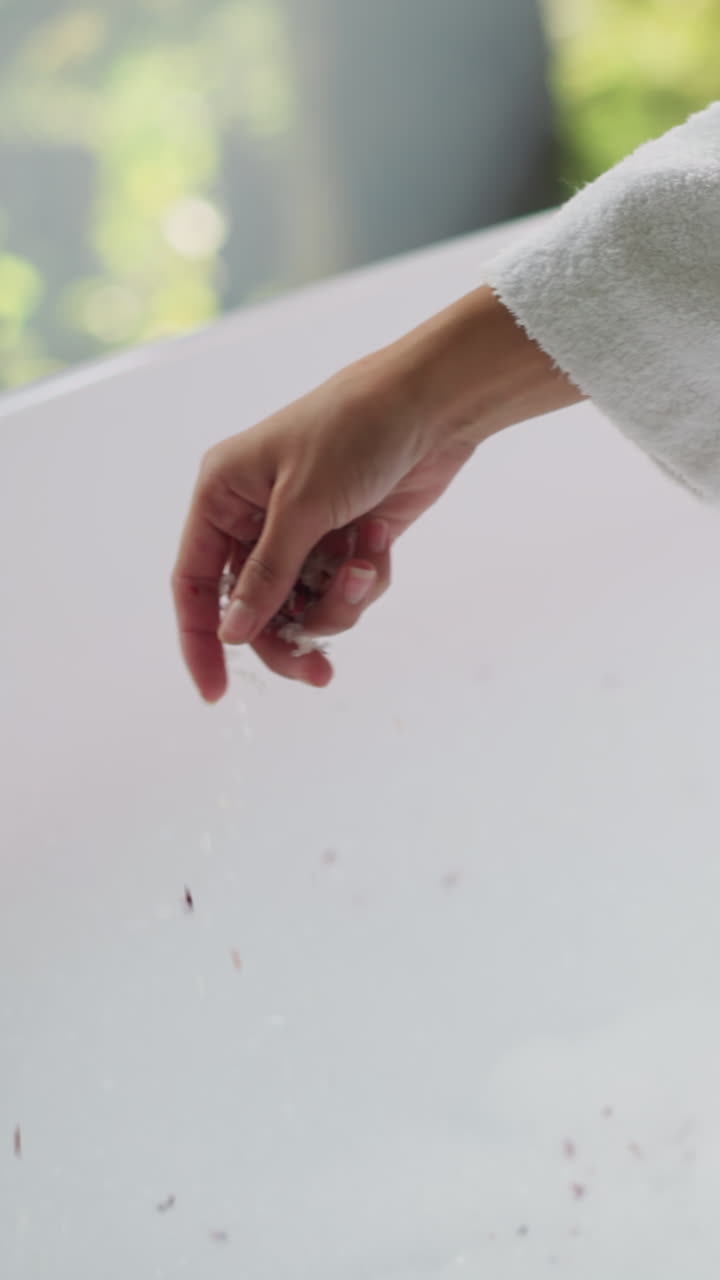 부인은 건조한 잎자루와 함께 욕조에 소금을 부어 부드러운 테리 욕조를 입은 여자가 뜨거운 물에 향기로운 성분을 첨가하여 목욕 절차를 준비합니다.