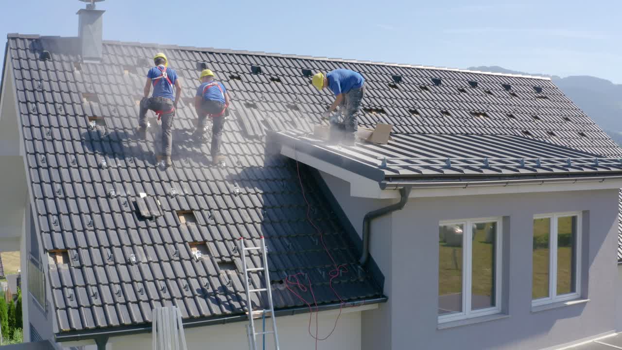 Construction Workers Installing Tiles On Roof Of Suburban House