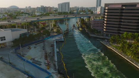 Forwards-tracking-of-ship-passing-under-highway-bridge-in-modern-city.-Scene-lit-by-late-afternoon-sun.-Miami,-USA