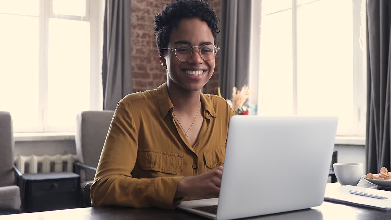 Smiling African woman texting on laptop pose at camera