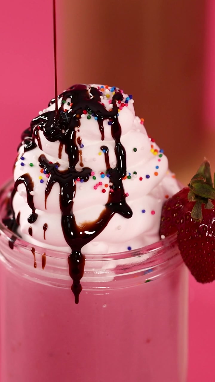 Primo piano di salsa al cioccolato che cola su panna montata e codette su un milkshake rosa.