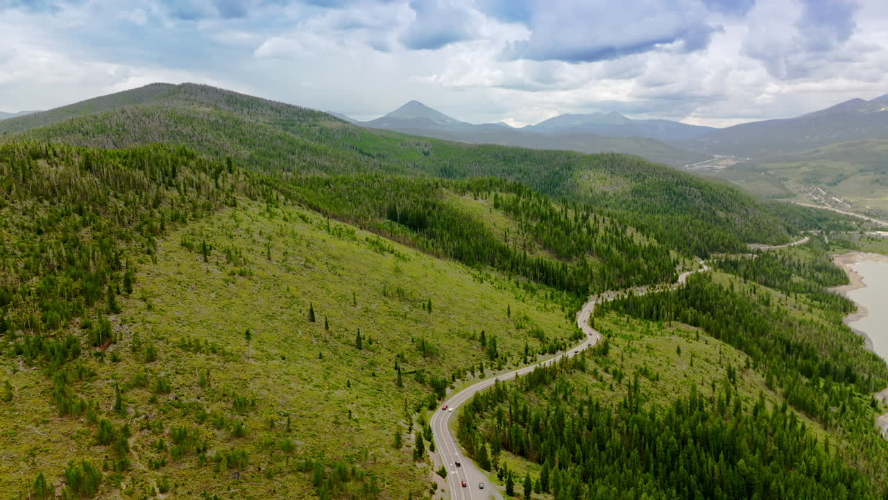 Green mountainous territories covered with fir-trees and grass. Highway in the hills nearby the mountain river. Cloudy sky at backdrop.