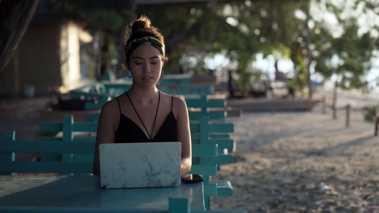 Ragazza freelancer che pensa al suo prossimo post sui social media al laptop in spiaggia, a Bali.