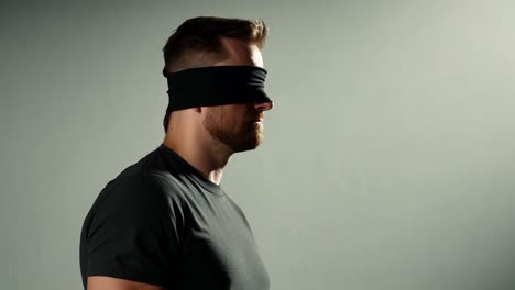 man wearing a black blindfold stands confidently against a gray background, creating an air of mystery and intrigue