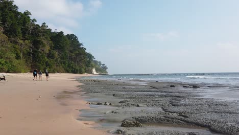 Zeitlupe-Mit-Kamera-Am-Strand-Entlang-Bei-Ebbe-Auf-Den-Andamaneninseln-Mit-Drei-Personen-Und-Einem-Hund-In-Der-Ferne-Und-Einem-Wald,-Der-Den-Abgelegenen-Strand-Säumt