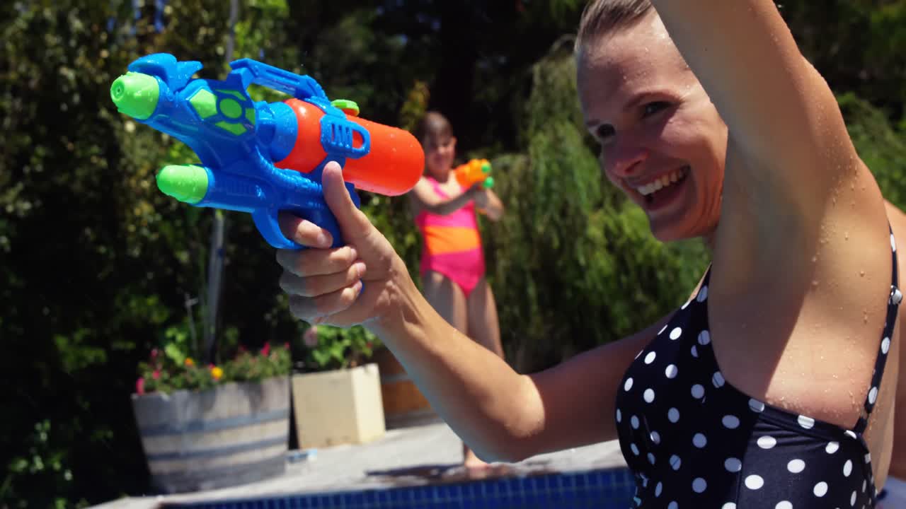 familia feliz haciendo una batalla de pistolas de agua en la piscina