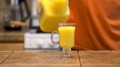 Man-in-orange-shirt-pouring-orange-juice-for-breakfast,-Closeup