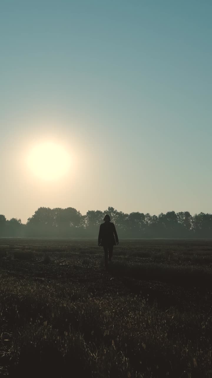Silhouette of Person Walking Towards the Sunrise in a Field