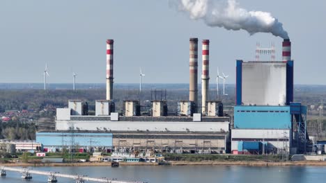 aerial-close-up-of-power-plant-with-white-smoke-smog-co2-released-from-chimney,-wind-turbine-producing-green-natural-energy-in-background