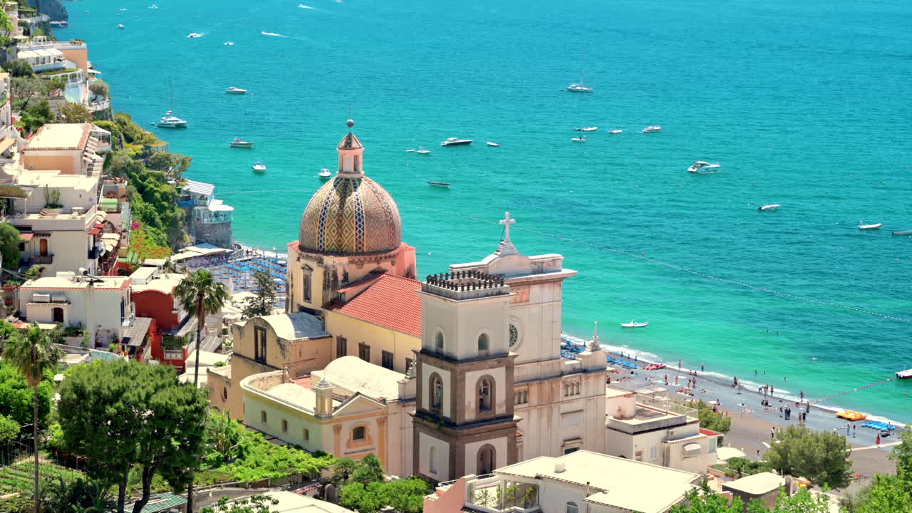 Paesaggio urbano di Positano, situata sulla costa del Mar Tirreno, Italia. File di edifici residenziali, chiesa, vegetazione, spiaggia con persone che si riposano