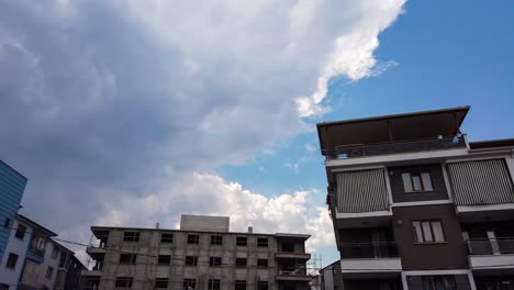 low angle shot in timelapse of dark rain and stormy clouds moving in blue sky over residential buildings at daytime