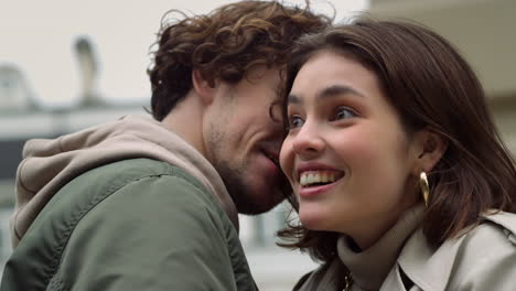 positive couple dating outdoor. man whispering secret to woman in city center.