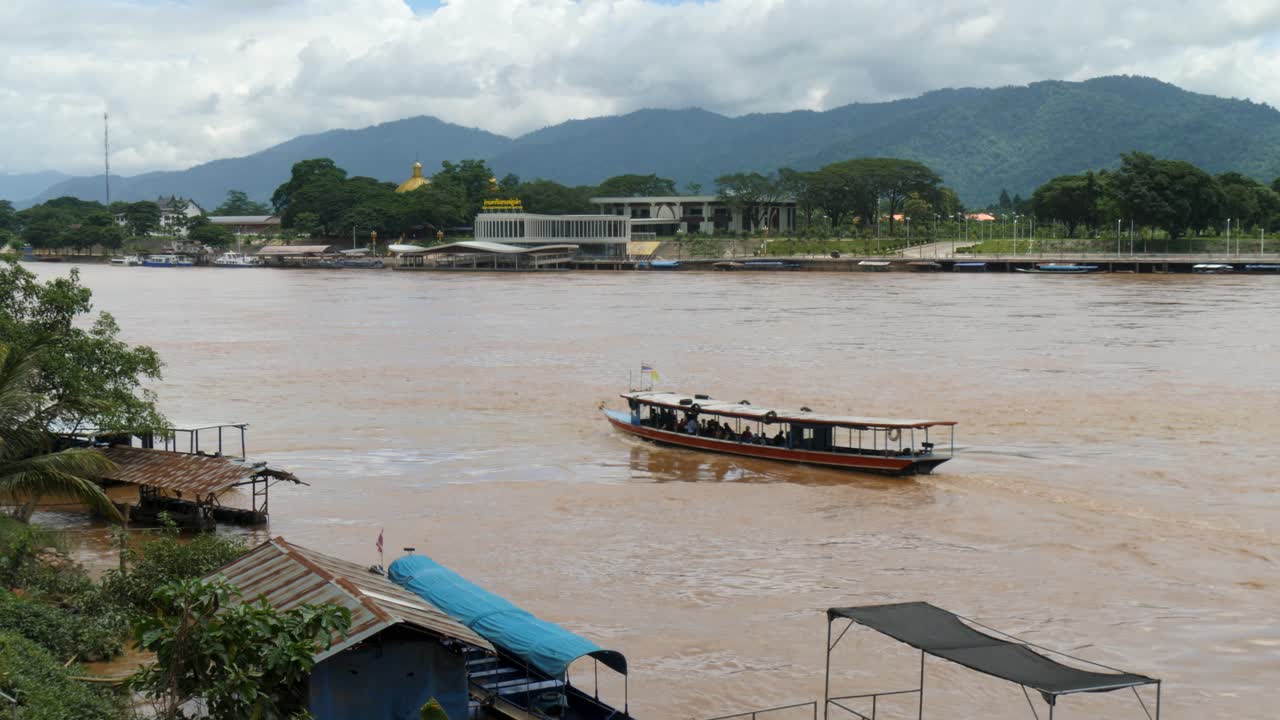 Mekong River with boat sailing between Thailand and Laos, surrounded by mountains and riverside settlements