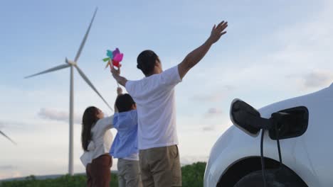 Concepto-De-Familia-Feliz-Progresiva-En-El-Parque-Eólico-Con-Vehículo-Eléctrico.