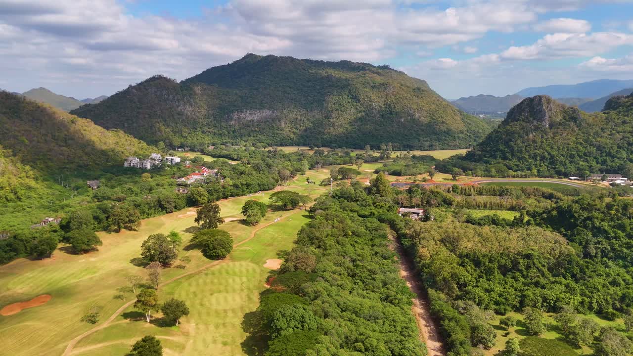 Toàn cảnh từ trên không bằng drone của một sân gôn xanh tươi, bao quanh là những ngọn núi đá vôi dưới ánh nắng mặt trời rực rỡ