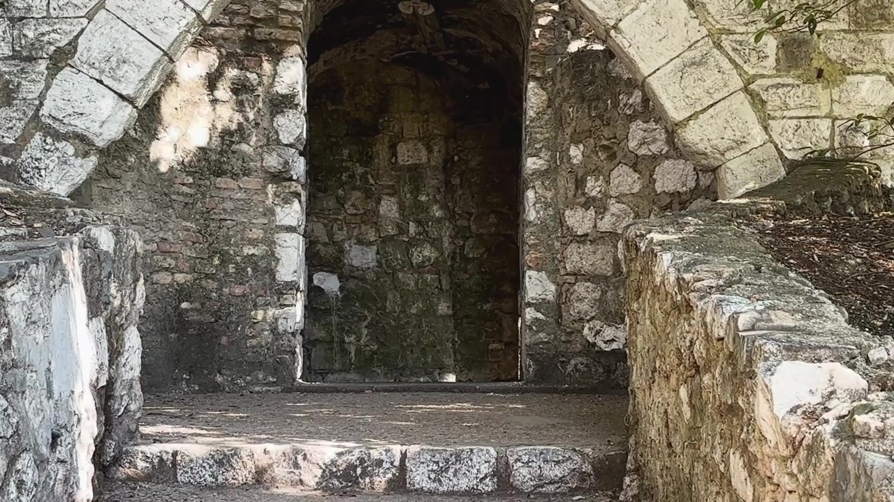 Arco de pedra desgastado e ruínas de alvenaria no Parc de la Colline du Château em Nice, França, cercado por arquitetura histórica sombreada