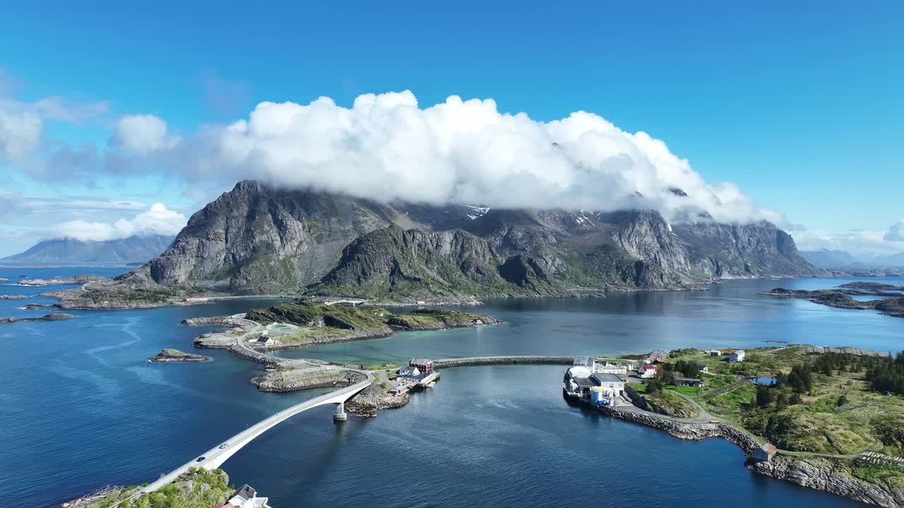 Drone flies forward over Henningsvaer road with bridges sea and mountains covered by clouds