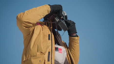 lower view of shutterbug adjusting lens on retro camera, gloved fingers fine tuning focus ring then pressing shutter trigger to capture crisp winter urban scene under bright sun