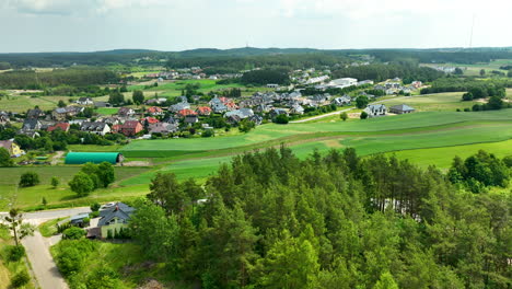 Aerial-view-of-a-rural-landscape-in-Iława,-featuring-a-small-village-with-residential-houses,-fields,-and-surrounding-forested-areas,-capturing-the-serene-countryside-atmosphere