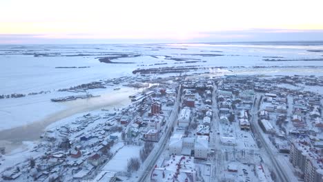 aerial view of a snowy siberian city by a frozen river at sunrise/sunset