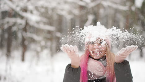 slow motion, a woman in a jacket hat and scarf in the winter in the forest holding snow in her hands and blowing into the camera throws snow.