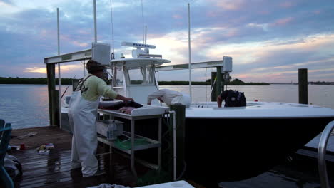 three fishermen clean docked sport fishing boat and fillet large game fish, sunset, slow motion