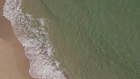 aerial pov with clear tropical ocean with small slow motion waves breaking on the sand