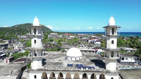 flying over old white mosque with two minarets and dome and surrounding neighborhood, mosque d'iconi in grande comore, comoros