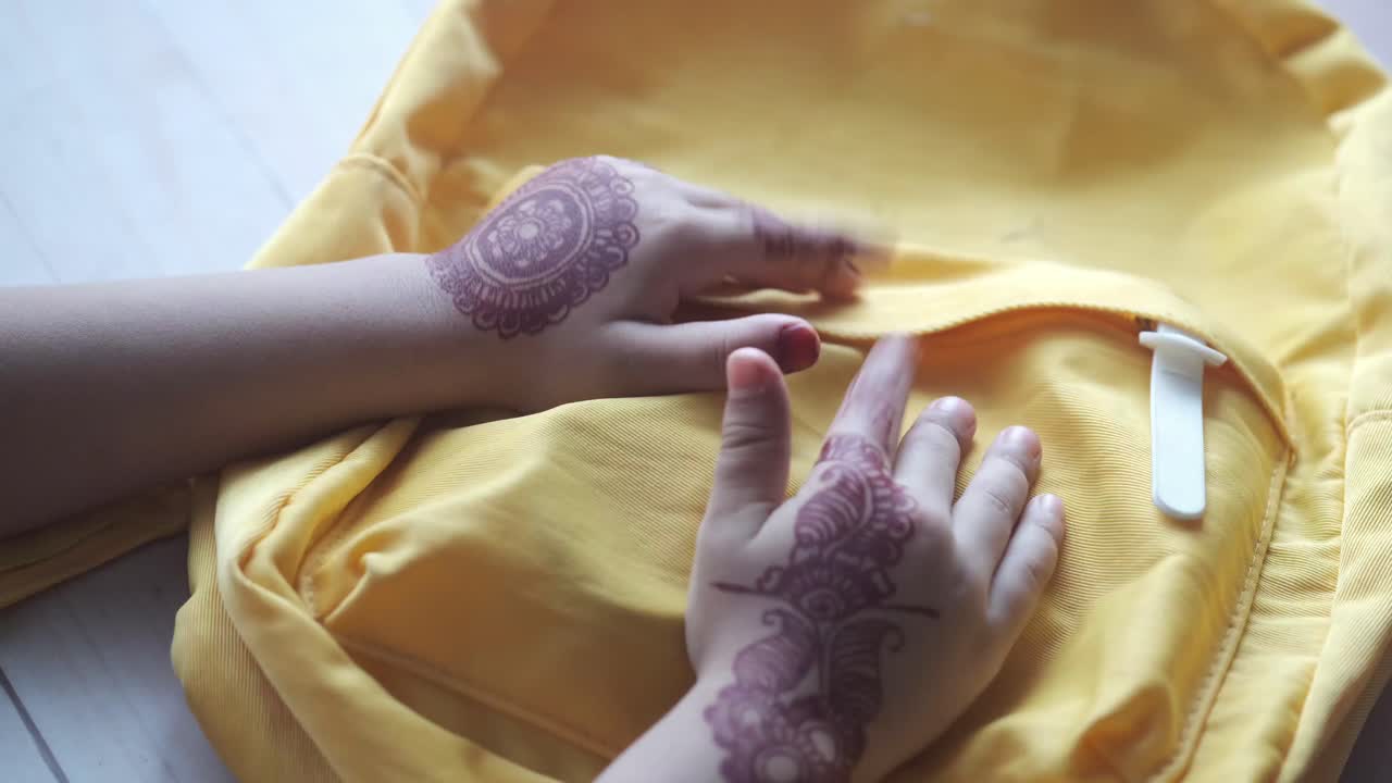 Mani di bambino con l'henné che decorano uno zaino giallo