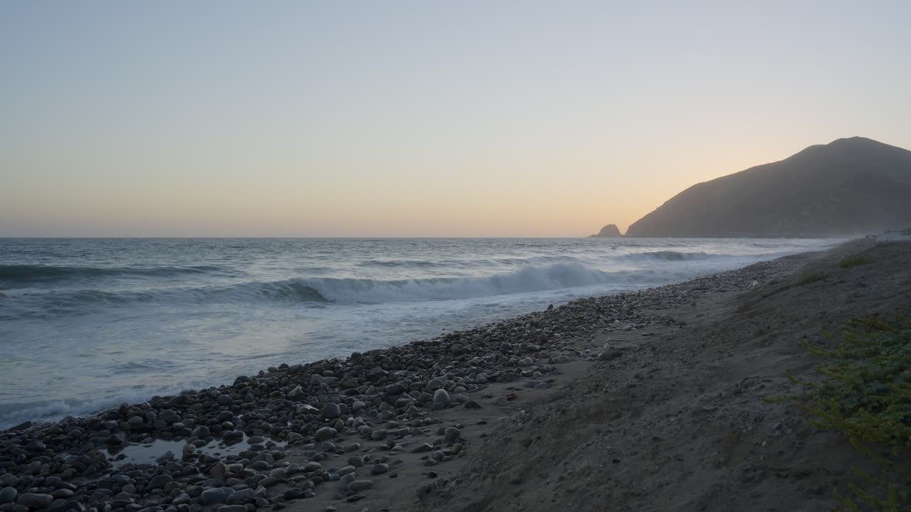 toma estacionaria de olas rompiendo en las rocas de la playa de mondo con puesta de sol detrás de la montaña en el fondo ubicada en el sur de california